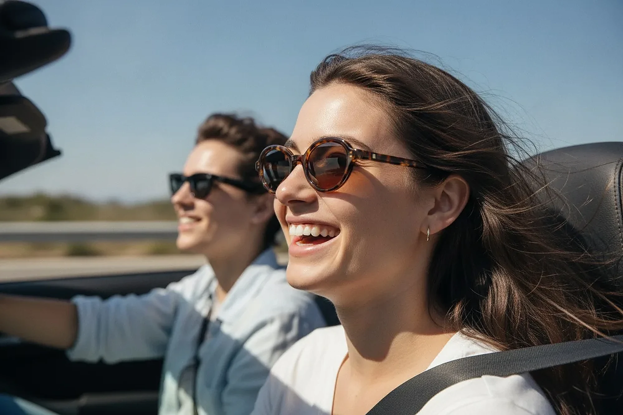 Un couple souriant portant des lunettes de soleil, en décapotable