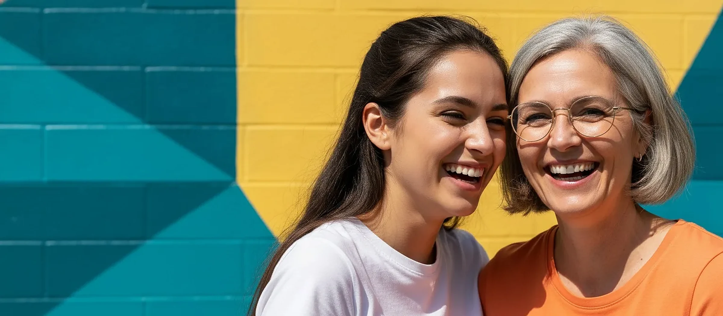 Deux femmes souriantes portant des lunettes, mur jaune et bleu