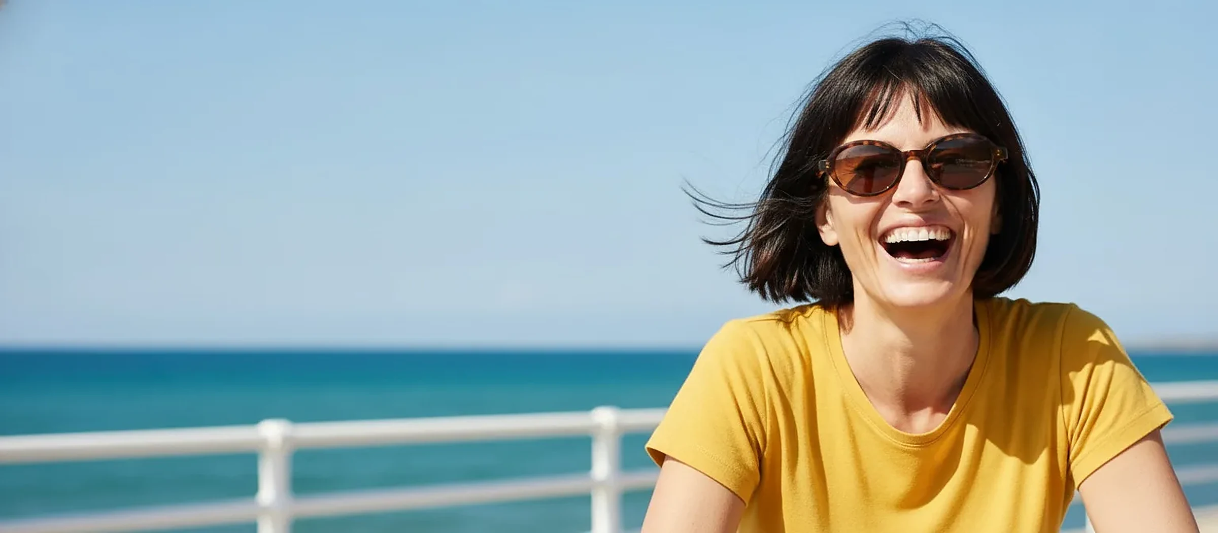 Femme riant aux cheveux courts et lunettes de soleil en écaille, fond mer