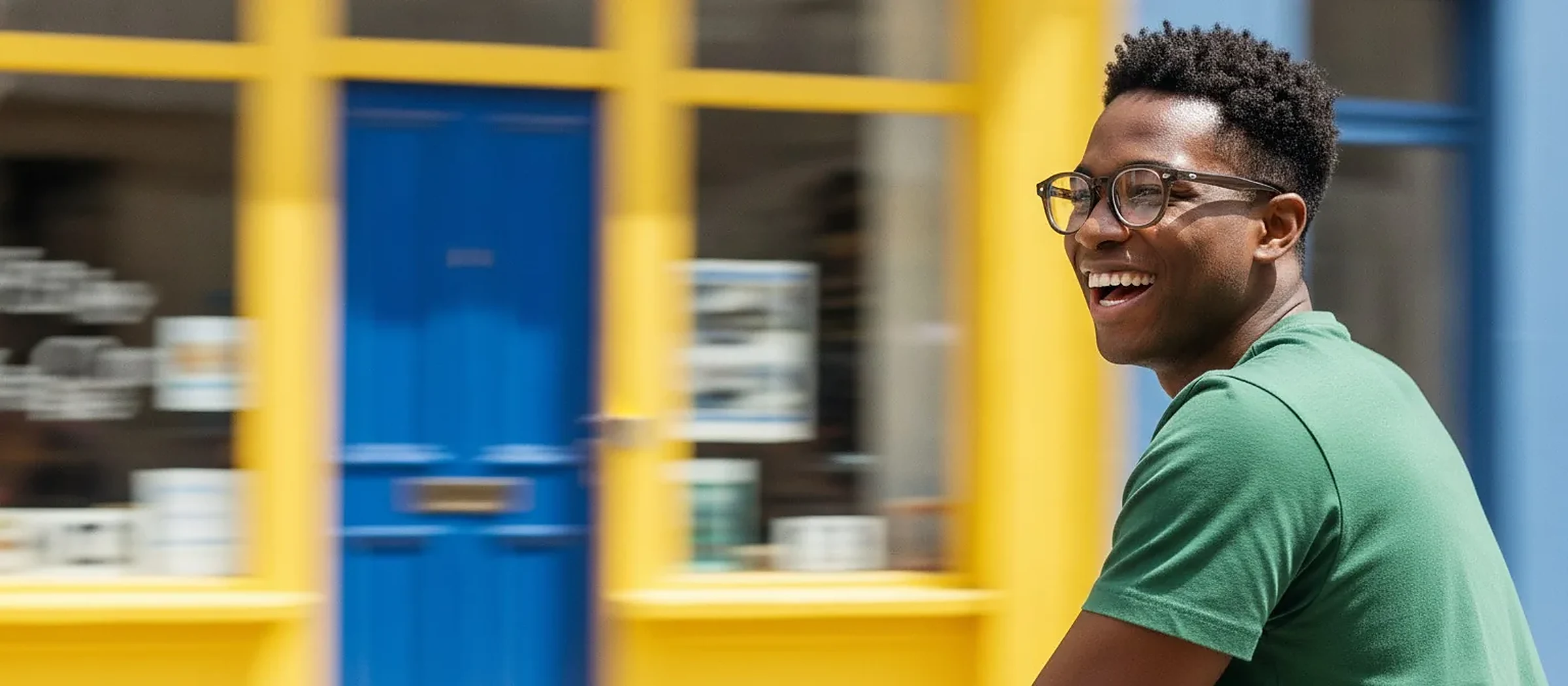 Homme souriant portant des lunettes, devant une porte bleue