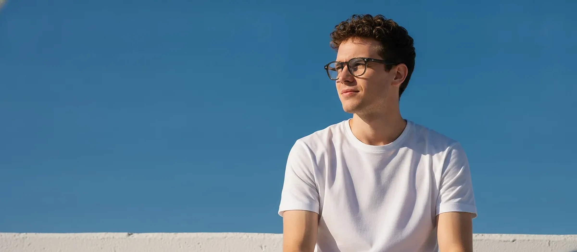 Homme aux cheveux bouclés portant des lunettes, fond ciel bleu