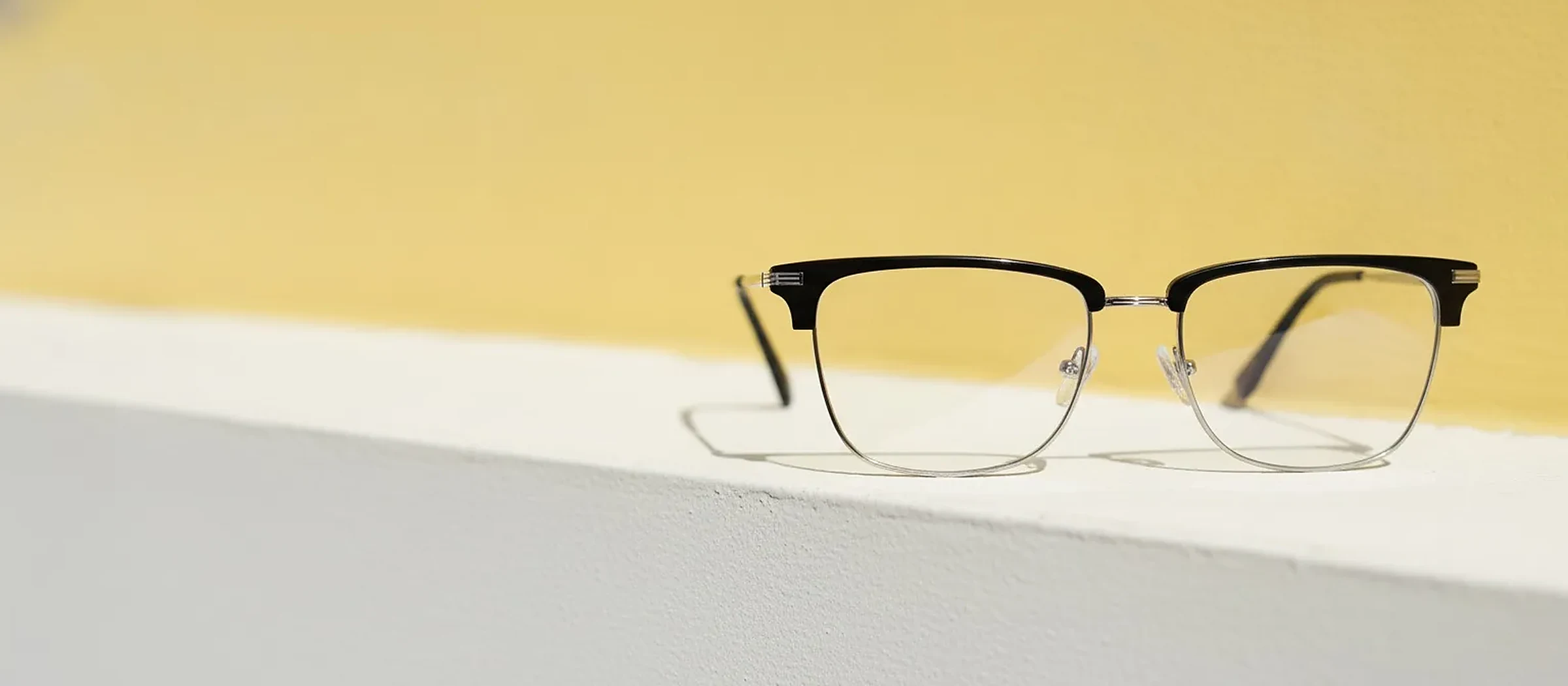 Lunettes clubmaster noires posées sur un rebord blanc, fond jaune