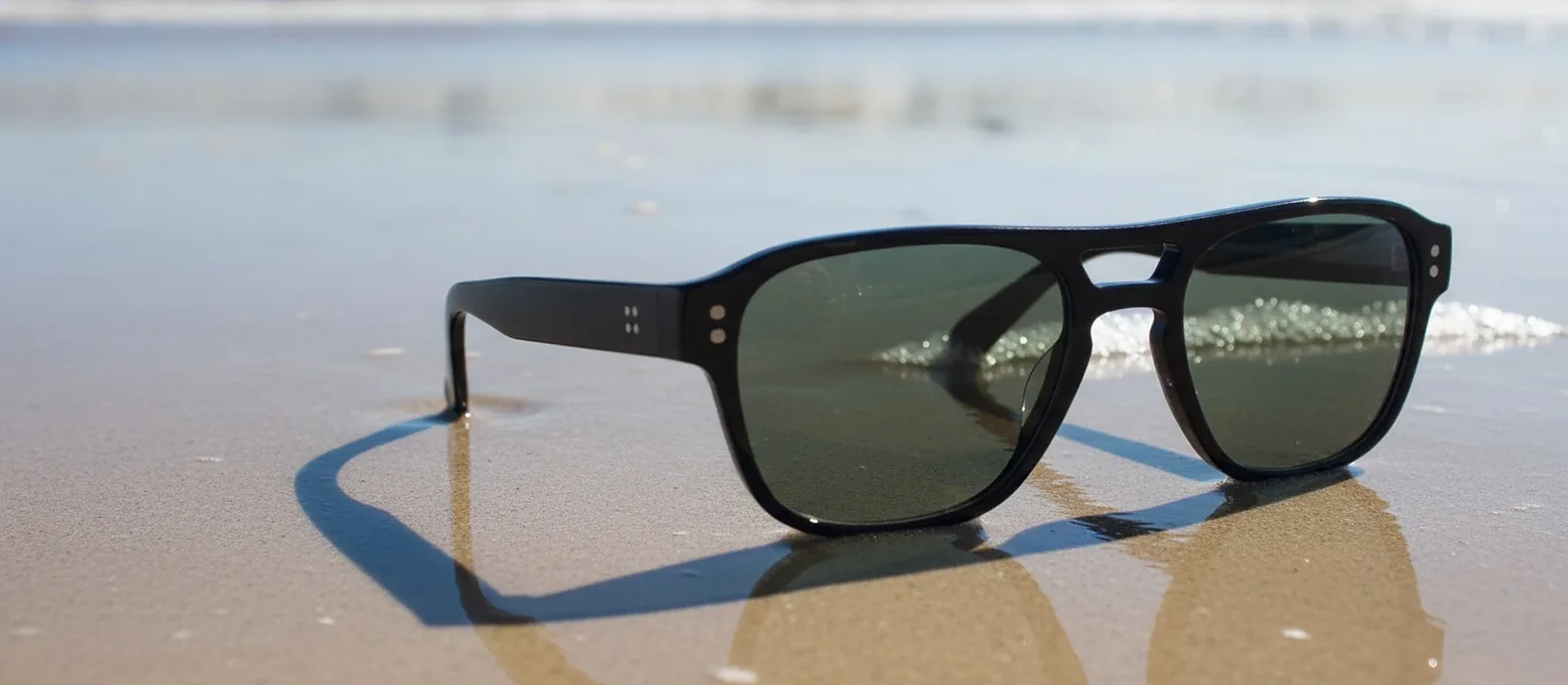Lunettes de soleil noires posées sur le sable, au bord de l'eau